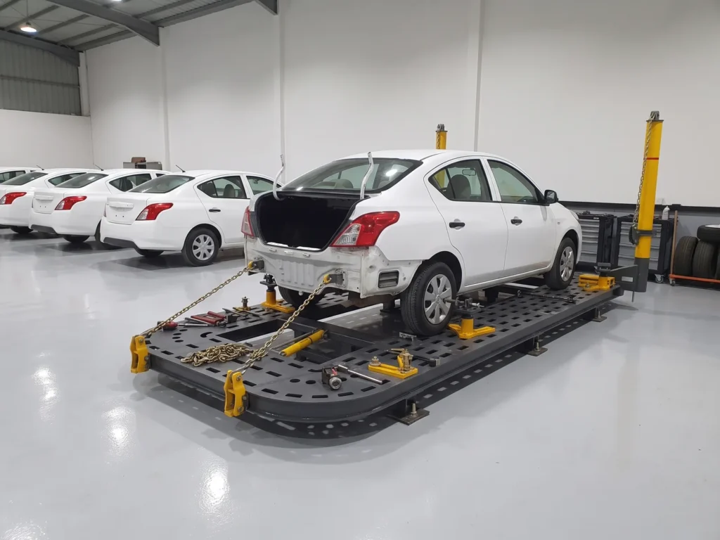A car with its rear bumper removed on a chassis puller, pulling chains on its rear, at a rental company