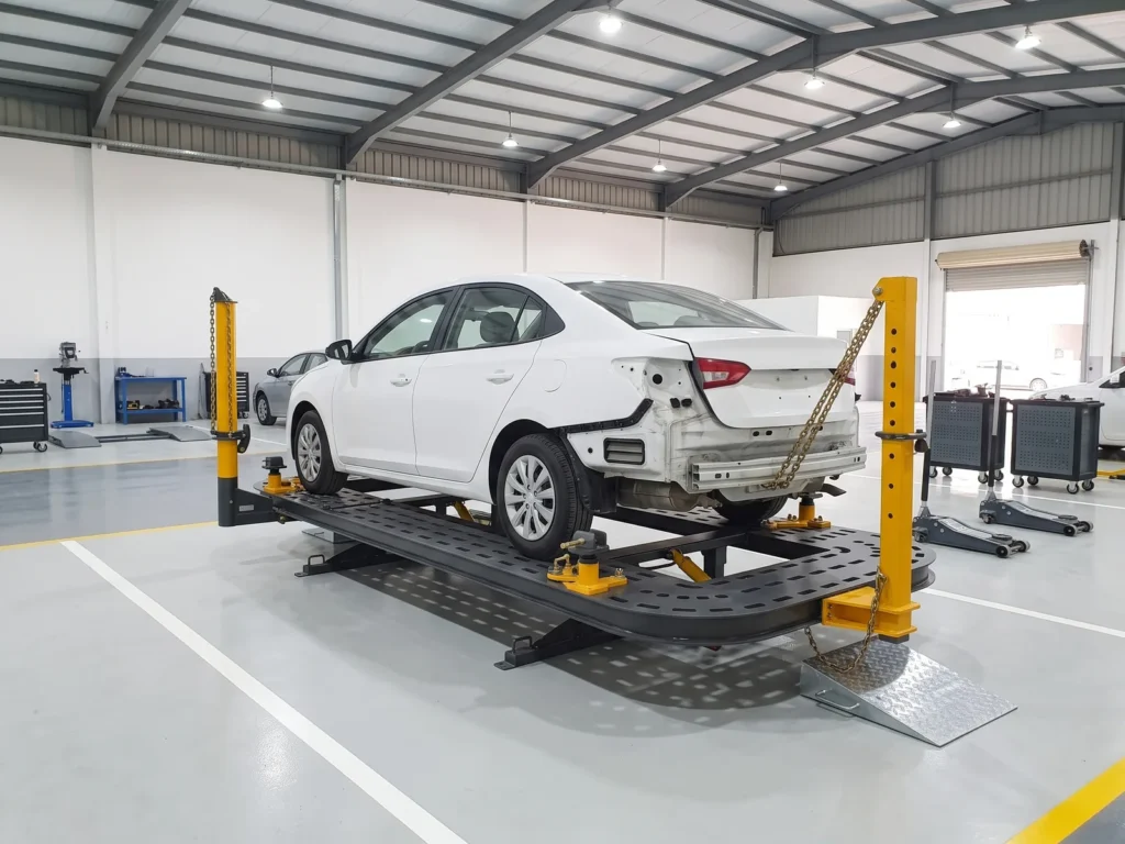 A car clamped on a chassis puller with a pulling tower chained to its rear in a repair workshop