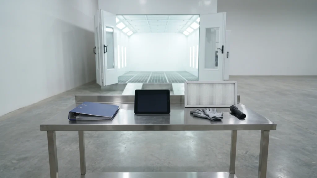 Maintenance binder, tablet, new filter and gloves on a workbench in front of a paint booth