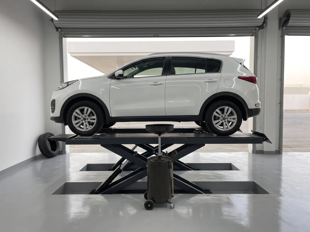 A car on a low scissor lift with an oil drain pan beneath it in a quick-service bay at a fuel station