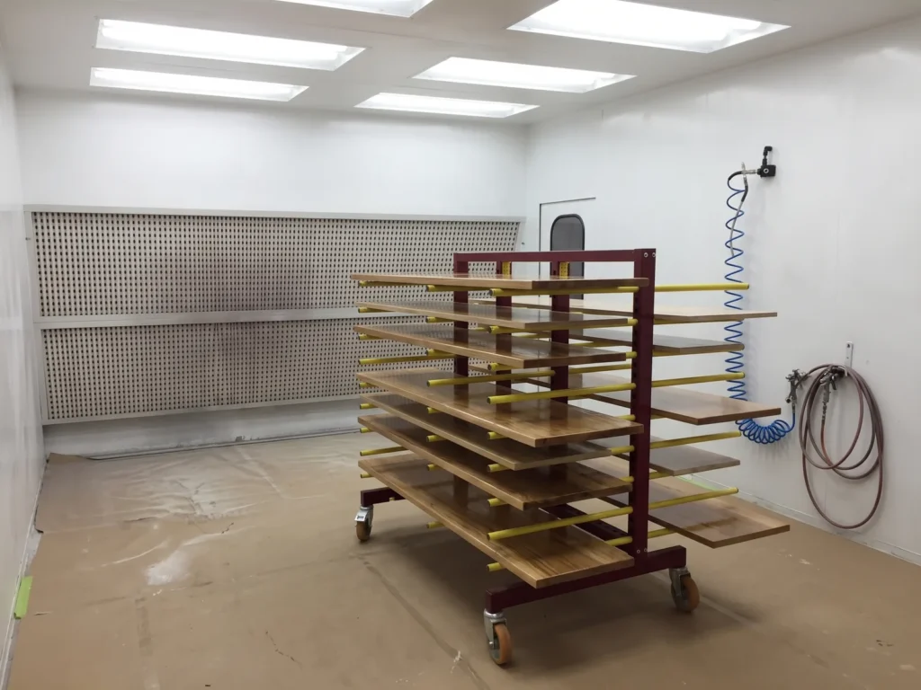 Lacquered wooden panels drying on a wheeled rack inside a finishing booth with a filter wall