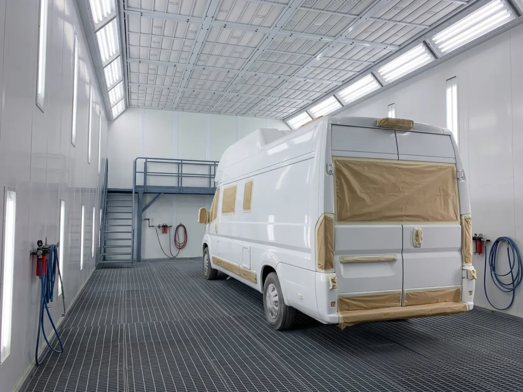 White motorhome with masked windows inside a large-vehicle paint booth