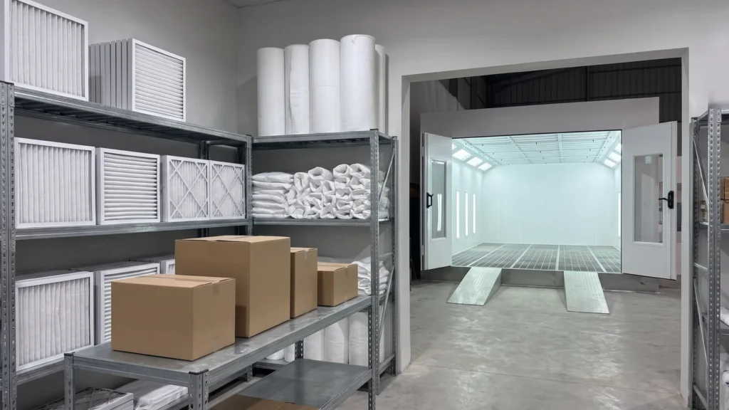Spare-parts store with new air filters and ceiling filter rolls, and the paint booth visible through the doorway