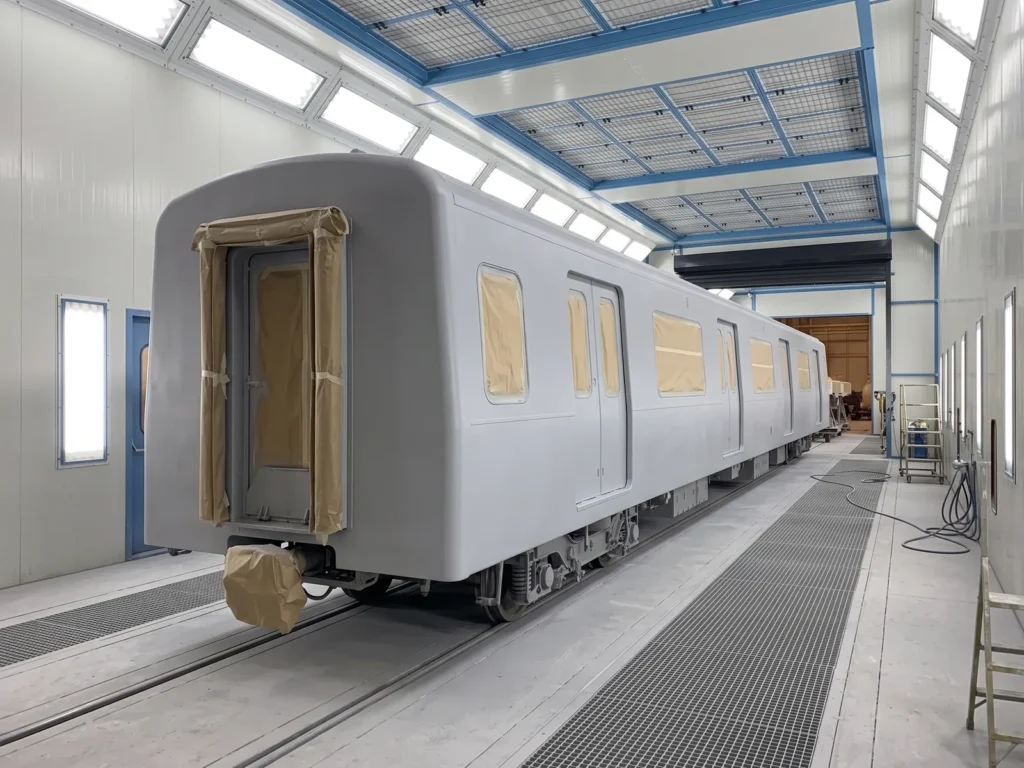 Passenger rail carriage in primer with masked windows inside a rail-size paint booth